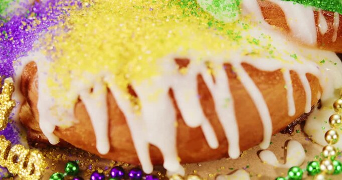 Decorated Mardi Gras king cake with gold, green, and purple sugar sprinkles. Authentic homemade kingcake to celebrate Mardi Gras with shiny beads and glittering yellow Happy Mardi Gras text.