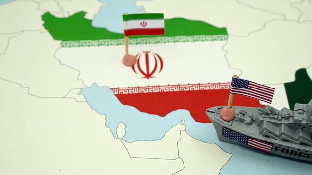United States and Iran national flags on a geopolitical map with a toy warship, representing a potential military conflict or diplomatic tension between the two countries