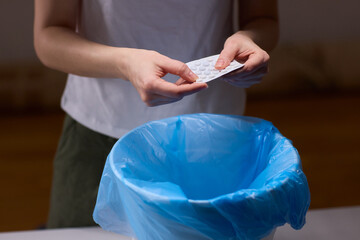 Hands discarding expired pills into bin, closeup of blister pack over blue plastic liner, tabletop...