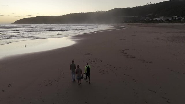 Drone follows three men walking along the beach at sunset on the Garden Route in Wilderness, South Africa