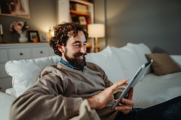 Smiling man relaxing on sofa using digital tablet