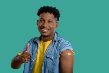 Young man shows his arm with a bandage after vaccination and gives a thumbs-up.