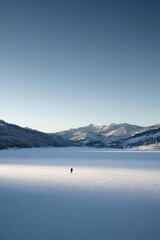A lone figure stands on a vast frozen lake, snow-covered mountains in the distance under a clear blue sky. Concept Lone figure on a vast frozen lake, Snow-covered mountains in the distance