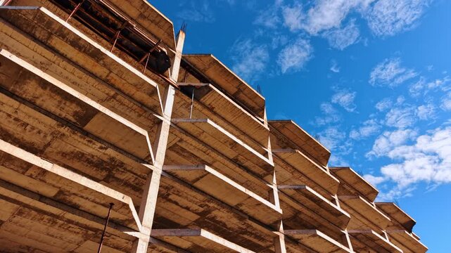 A view of an incomplete concrete structure seen from below, capturing the various levels of the building. The cloudy sky above contrasts with the raw textures of the concrete.
