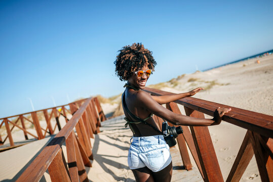 Photographer walking down wooden bridge at beach smiling at camera