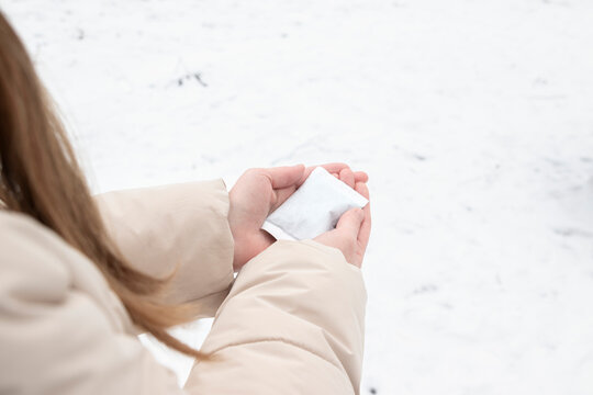 Woman holding a disposable hand warmer while standing outdoors in winter. Concept of cold weather readiness, thermal comfort, outdoor lifestyle, seasonal protection.