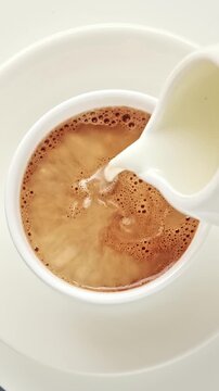 Milk cream is poured into a cup black morning coffee cup. Top view, flat lay. Vertical 