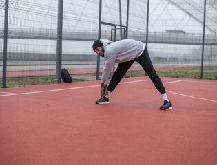 Young athletic man stretching legs during warm-up on an outdoor basketball court. Focused fitness training, flexibility exercise, urban sports lifestyle and healthy active living