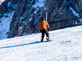 Man in an orange jacket is snowboarding down a mountain