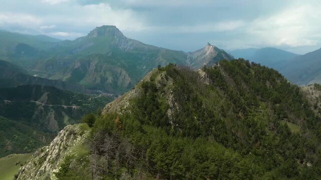 aerial footage captures the stunning natural beauty of the Zalala Ridge in the Republic of Dagestan. The camera glides over a forested ridge, revealing a dramatic landscape of rolling green hills, dee