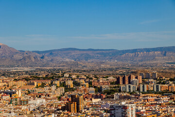 Naklejka premium A vast cityscape stretches towards distant mountains under a clear blue sky.