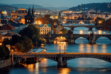 Obraz premium Cityscape At Dusk With Glowing River Bridges, Warm Streetlights Shine On Peaceful Vltava River Arches