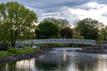 Long white metal footbridge crossing the Rideau River. Arched pedestrian bridge in scenic Ontario park setting