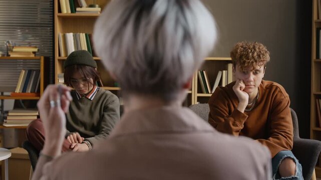 Professional female therapist listening to frustrated teenage couple quarrelling during shared counseling meeting in therapy room