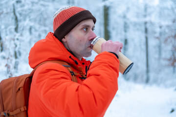 Happy backpacker man in orange jacket drinking hot tea from thermos in snowy forest during winter walk, cozy outdoor break, cold season travel and healthy lifestyle, winter getaway and quality time