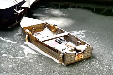 anchored small wood fishing boat and paddle frozen in ice. winter scene. large boat nearly. season specific image. detail at the river side. yellow tie rope coiled up.