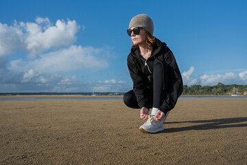 sporty woman runner tying her shoe, training on the beach