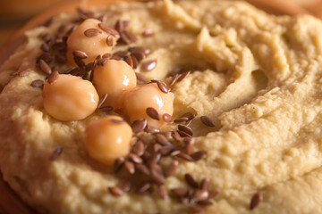 Close up of creamy hummus texture topped with organic chickpeas flax seeds and olive oil in a bowl