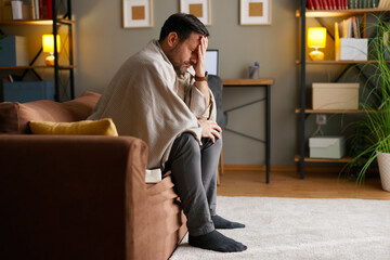 Man suffering from headache and illness while sitting on a couch at home