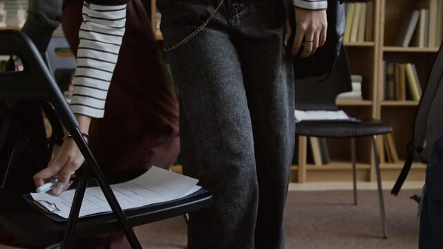 Cropped shot of teenage learners entering college counselling office then picking up clipboards from chairs and filling out emotional health questionnaires during group session