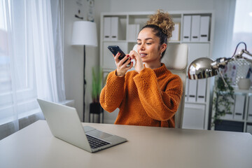 Woman recording voice message on smart phone working at home office