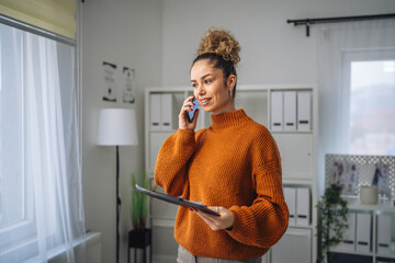 Woman working and smiling while talking on phone and holding document