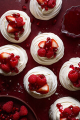 Mini pavlova cakes topped with whipped cream, fresh berries and berry sauce
