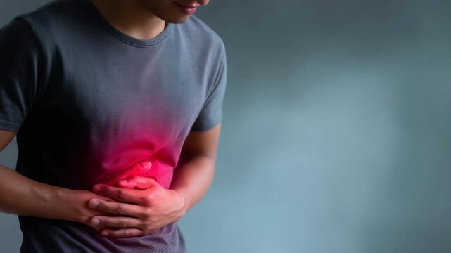 high-resolution medical-themed photograph showing a man wearing a gray T-shirt, bending slightly forward and holding his abdomen with both hands, indicating discomfort or abdomin 4K