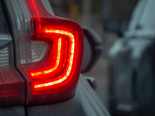 Close-up of a modern red LED car taillight illuminated at dusk with a shallow depth of field and soft bokeh background.