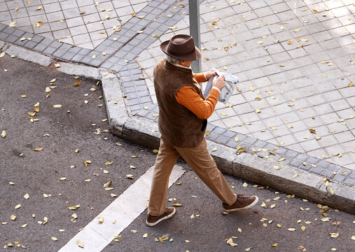 Se&ntilde;or elegante con clase, estilo, sombrero y chaleco cruzando calle y abriendo paquete