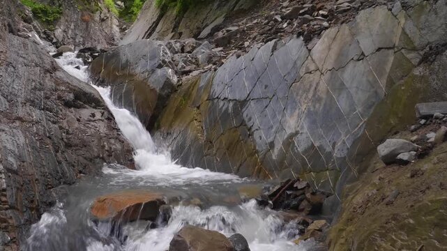 Footage captures the serene natural beauty of the Zryh Waterfall in the Republic of Dagestan, Russia. A clear mountain stream flows dynamically over a series of rugged, wet grey rocks and boulders nes