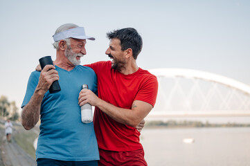 Father and son smiling and holding water bottles after exercising outdoors