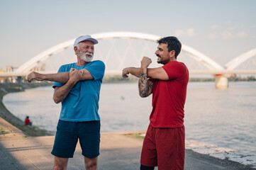 Senior man and personal trainer stretching before exercising by the river