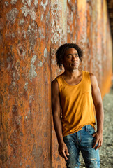 A young handsome man,an African model, walks alone, in a yellow T-shirt and jeans, in an unusual place