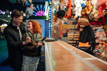 Happy couple enjoying shooting gallery game at amusement park