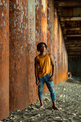 A young handsome man,an African model, walks alone, in a yellow T-shirt and jeans, in an unusual place