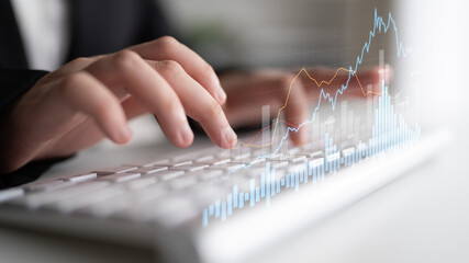 Close-up of hands typing on a keyboard with a digital graph overlay, illustrating financial data analysis and business growth in a modern office setting. Scalp