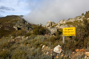 Translation: Military zone, no entry, danger of explosions. Information sign in a mountainous area, yellow in color, warning of the boundaries of a military exercise zone.