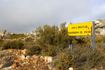 Translation: Military zone, no entry, danger of explosions. Information sign in a mountainous area, yellow in color, warning of the boundaries of a military exercise zone.