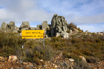 Translation: Military zone, no entry, danger of explosions. Information sign in a mountainous area, yellow in color, warning of the boundaries of a military exercise zone.