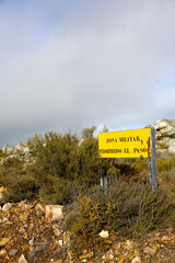 Translation: Military zone, no entry, danger of explosions. Information sign in a mountainous area, yellow in color, warning of the boundaries of a military exercise zone.