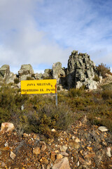 Translation: Military zone, no entry, danger of explosions. Information sign in a mountainous area, yellow in color, warning of the boundaries of a military exercise zone.