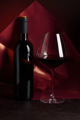 Red Wine Bottle and Glass on Dark Red Gradient Background. Elegant Still Life