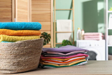 Laundry basket with towels and clothes on wooden table indoors, closeup. Space for text