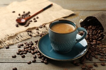 Aromatic coffee in cup and roasted beans on wooden table, closeup