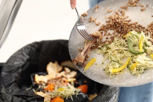 Woman throwing food waste into garbage can in kitchen, closeup