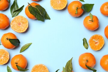 Fresh ripe tangerines and green leaves on light blue background, flat lay. Space for text