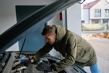 Man inspecting car engine under open hood in residential garage