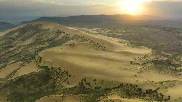 aerial drone footage showcases the majestic Sarykum Dune at sunset. This barchan is the highest sand dune in Europe and a protected area within the Dagestan Nature Reserve. The golden sands contrast b