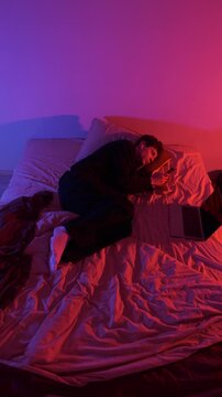 Man scrolling on phone in bed then laying curled up in different moments, changing scenes showing digital fatigue, online chatter, modern routine, generation z and millennial lifestyle. Vertical video